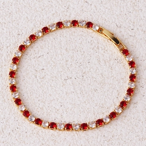 Detail van gouden tennisarmband met afwisselend rode en heldere zirkonstenen en sluiting