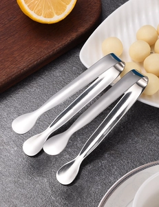 Polished stainless steel sugar tongs arranged on a dark stone surface with food props