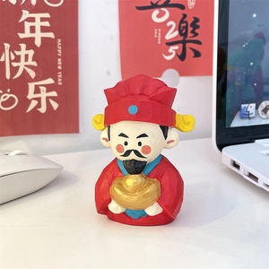 Close-up of hand-carved red God of Wealth figurine with gold ingot on a desk