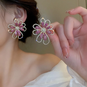 Detailed view of oversized gold flower earrings with pink and clear crystals on model