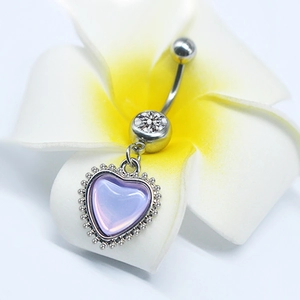 Macro shot of heart-shaped purple resin navel piercing on white plumeria flower