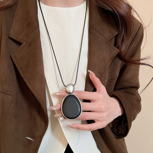 Gros plan d'un grand pendentif ovale noir sur collier long porté sur un manteau marron