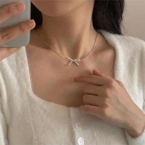 Close-up of elegant bow pearl pendant necklace on a gold chain worn by a model