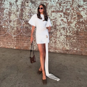 Detail of white mini dress featuring side draped ribbon and decorative waist buckle detail