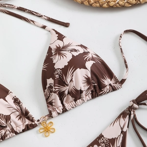 Detail of hibiscus print bikini top with golden flower charm on white stone background