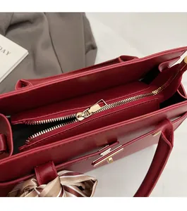 Detail of red leather tote bag showing smooth gold zipper closure and silk scarf