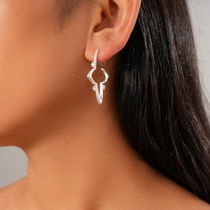 Macro close-up of a silver geometric starburst earring worn by a model in soft light
