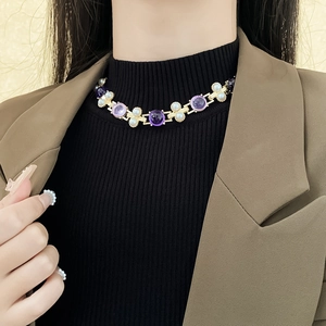 Collier vintage doré avec pierre violette et perles blanches sur un mannequin en veste brune