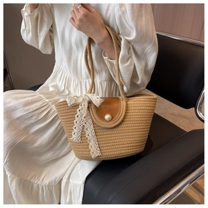 Detail of straw tote bag with brown leather flap, lace bow, and pearl buckle closure