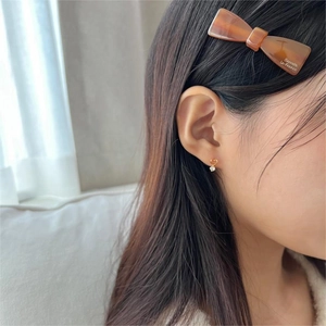 Close-up of heart-shaped zircon stud earrings worn with a brown bow barrette clip