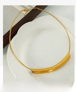 Detail of 18k gold plated stainless steel curved tube necklace on a white ceramic plate