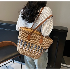 Close-up of woven straw tote bag with colorful base and brown leather shoulder straps