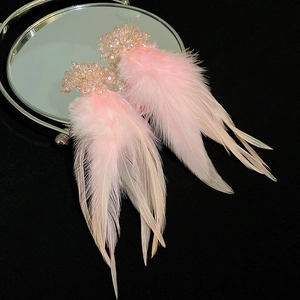 Macro shot of pink crystal cluster earrings with soft feather tassels on a mirror