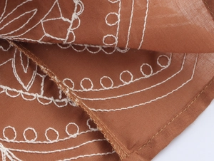 Détails des broderies blanches et de la texture du tissu sur une robe marron sans manches