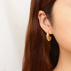 Close-up of golden C-shaped stud earrings with textured dot pattern on female model