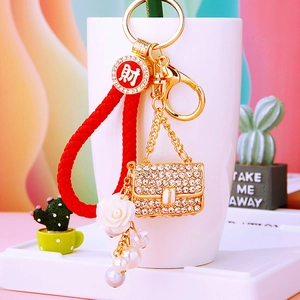 Detail of red braided keychain with rhinestone mini bag, rose charm and fortune coin tag