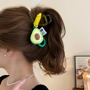 Detail of cute avocado hair clip and yellow hair tie worn by a model in a cozy setting