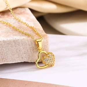 Macro detail of gold-plated double heart necklace with sparkling zircon pavé on beige stone