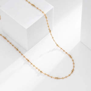 Detailed view of delicate gold S925 sterling silver bead chain on a white display block