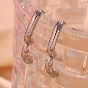Macro shot of polished silver hoop earrings hanging on a textured glass rim