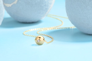 Macro shot of a golden spherical pendant necklace featuring a brilliant round-cut diamond
