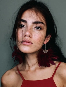 Close-up of deep red feather earrings with golden metal base worn by a model