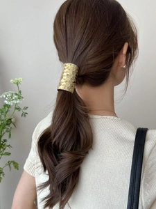 Detail of golden hair clip with honeycomb hammered texture on model's ponytail