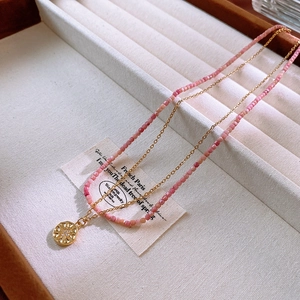 Detail of pink square beads and a golden celestial pendant on a double-layer necklace