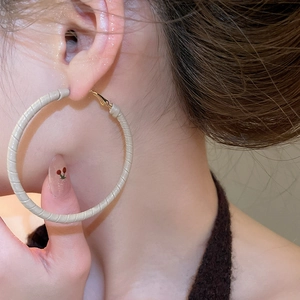 Macro detail of beige leather wrapped golden round hoop earring worn by a model