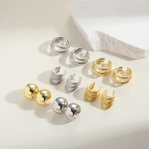 Detailed close-up of gold and silver minimalist clip-on earrings on white stone props