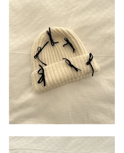 Close-up of cream knit beanie featuring delicate black velvet ribbon bow details