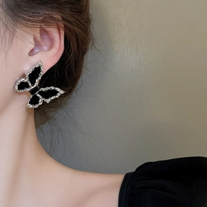 Detail of silver-edged black butterfly earrings worn by a model in soft lighting