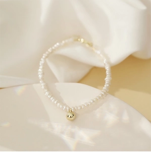 Detail of natural white pearl necklace with gold sphere pendant on ceramic dish