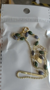 Dettaglio di un bracciale a doppio strato dorato con perle verdi e viola confezionato