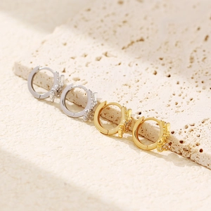 Macro shot of silver and gold butterfly hoop earrings with crystals on a beige stone