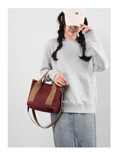Detail of a thick canvas shoulder bag in burgundy with khaki straps on a model