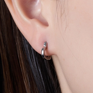 Close-up of a polished silver heart huggie earring worn on the earlobe with a soft focus