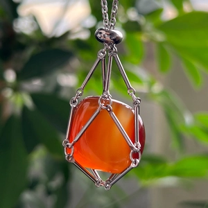 Close-up of raw orange crystal pendant in silver metal cage on a natural green background
