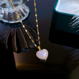 Detailed close-up of heart pendant with iridescent stone and pavé zircon on gold leaf chain