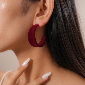Close-up of a burgundy velvet C-shaped earring worn on a model's ear for autumn style