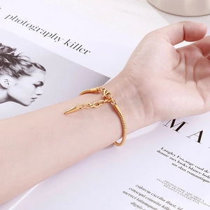 Detail of golden snake chain bracelet with spiked charms worn on a fashion background