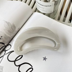 Detail of a glossy greyish-white crescent hair claw clip on an artistic magazine