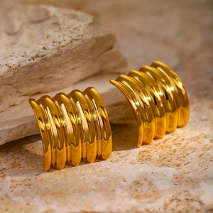 Detail view of gold 18k wavy square stud earrings on natural beige stone background