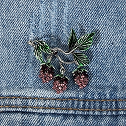 Detailed view of berry and leaf brooch with dark crystals on blue denim fabric