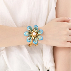 Close-up of golden flower cuff bracelet featuring blue enamel petals and a central pearl