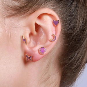 Macro shot of gold and purple enamel heart, moon, and smile stud earrings on ear
