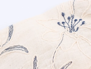 Macro shot of beige linen fabric texture with dark blue floral embroidery detailing