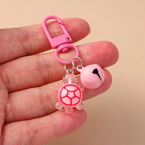 Pink resin turtle keychain with metal bell and lobster clasp held in hand