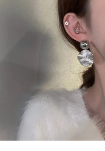 Gros plan d'une boucle d'oreille géométrique argentée avec disque texturé sur l'oreille