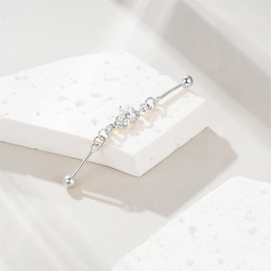 Detail of silver S925 industrial piercing bar with clover design on stone surface
